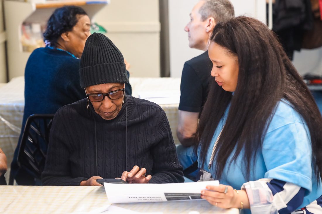 A volunteer helps a senior in a beanie with her phone